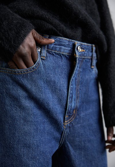Denim jeans in een diepblauwe kleur met contrasterende oranje stiksel. Ontworpen met een klassieke pasvorm en een middelhoge taille, met voorzakken.