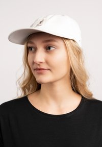 Cappellino bianco in cotone con visiera curva e logo ricamato sul fronte; indossato con una maglietta nera, caratterizzata da una consistenza morbida e un design casual.