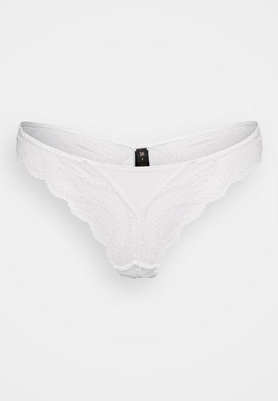 Tanga bianco in pizzo con un design testurizzato, bordi ondulati e un tessuto morbido. Presenta un piccolo etichetta nera sul retro.