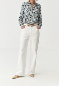 Květinová blůza v modré, černé a bílé barvě s límečkem. V kombinaci s bílými dámskými kalhotami se širokými nohavicemi a béžovými lodičkami s špičatou špičkou.