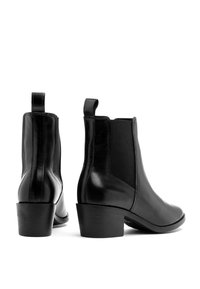 Czarne skórzane botki za kostkę z elastycznymi bocznymi panelami, zaokrąglonym noskiem i niskim obcasem typu blok. Wyposażone w pętelki ułatwiające zakładanie.
