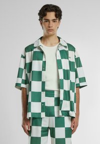 Camicetta a maniche corte con un motivo a scacchi verde e bianco, tessuto leggero, chiusura con bottoni davanti, abbinata a pantaloni a scacchi coordinati.