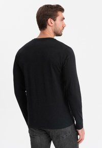 Camisa negra de manga larga hecha de tela suave, con un escote redondeado y un corte relajado, con costuras mínimas y etiquetas en el lateral.