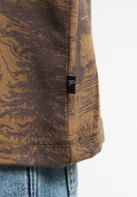 Bruine T-shirt met een abstract, donkerder patroon. Zachte stof, korte mouwen en een zijlabel met een blauwe achtergrond en witte tekst.