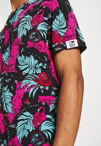 Kurzärmliges Hemd mit Druck auf schwarzem Hintergrund. Enthält lebendige pinke und türkisfarbene tropische Muster, darunter Blätter und Flamingos.