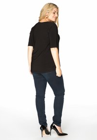 Sort kortærmet top med en afslappet pasform og rund halsudskæring, parret med mørkeblå slim-fit jeans og sorte lakhæle.