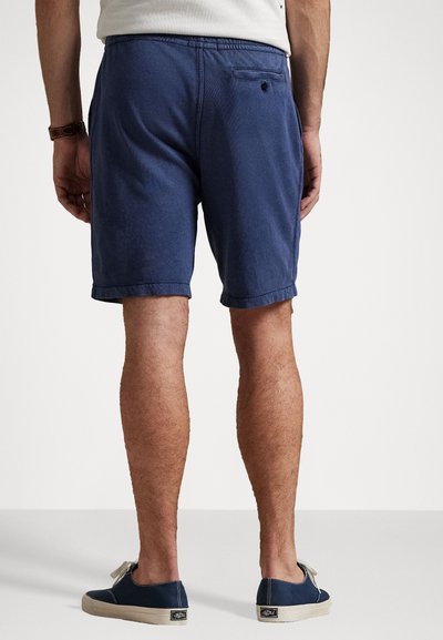 Shorts bleu marine avec une ceinture élastique, des manches retournées et une poche arrière. Portés avec des chaussures bateau en toile bleu marine.