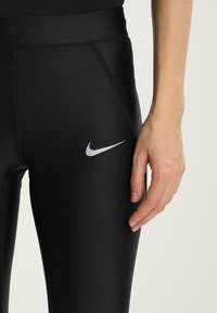 Czarne legginsy Nike z elastycznego materiału o dopasowanym kroju. Posiadają srebrne logo na lewej udzie oraz płaskie szwy.