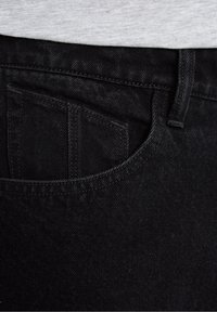 Black denim jeans featuring a front pocket with visible stitching, smooth texture, and a subtle sheen, partially covered by a grey shirt.