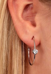 Orecchino a cerchio in argento con una pietra preziosa a forma di cuore nella parte inferiore, caratterizzato da una superficie liscia e lucida e da un design semplice ed elegante.
