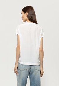 Weißes Kurzarm-T-Shirt mit lockerem Schnitt, leicht strukturiertem Stoff und rundem Halsausschnitt, kombiniert mit hellblauen Jeans.