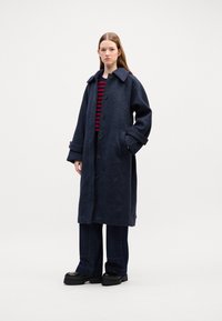 Cappotto di lana navy con ampio colletto, bottoni frontali, tasche laterali e vestibilità ampia. Abbinato a un top a righe rosse e nere e pantaloni in denim scuri.