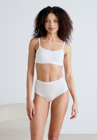 Valge puuvillane bralette ja kõrge vöökohtadega aluspükste komplekt, millel on sile tekstuur ja reguleeritavad rihmad, esitatud modellil neutraalses taustal.