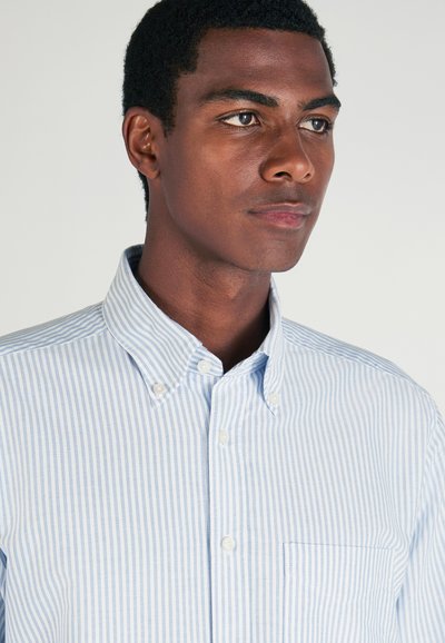 Camicia button-up a strisce azzurre e bianche con colletto appuntito, taschino sul lato sinistro del petto e tessuto di cotone testurizzato.