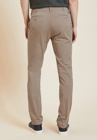 Chinos beiges avec une coupe slim, présentant une texture lisse, deux poches arrière et des détails de couture subtils, associés à des baskets marines.