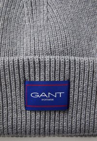 Gray knitted beanie with ribbed texture; features a blue tag with "GANT" and "SPORTSWEAR" in white text, surrounded by a red border.