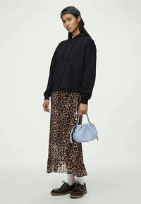 Črna skrajšana kapuca, maksi krilo z leopardjim vzorcem, modra torbica, bele nogavice, črne čevlje s srebrnimi detajli; sproščen outfit z mešanimi vzorci.