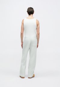 Λευκό ριμπ τοπ χωρίς μανίκια συνδυασμένο με ανοιχτό γκρι, άνετο παντελόνι φόρμας με πίσω τσέπη και ελαστική μέση. Καφέ υποδήματα.