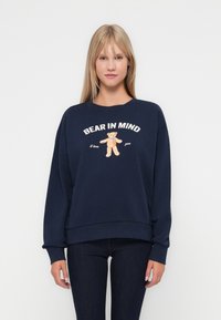Navy blue sweatshirt in soft material with a loose fit. Features a graphic of a bear and text "BEAR IN MIND I love you" in white and orange.