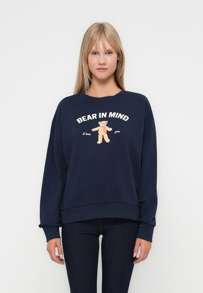 Marineblauwe sweatshirt van zacht materiaal met een losse pasvorm. Voorzien van een grafische afbeelding van een beer en de tekst "BEAR IN MIND I love you" in wit en oranje.