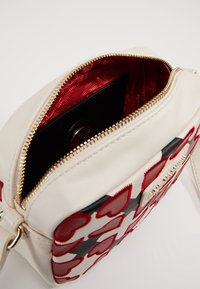 White leather bag with red heart patterns, gold zipper, and red satin lining, featuring a black interior pocket for organization.