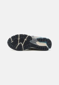 Sole modré a šedé běžecké boty New Balance, ukazující černý vzor podrážky a odpružení na bílém pozadí.