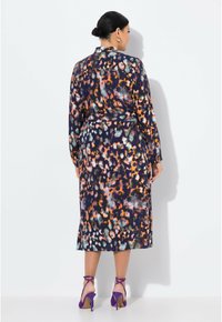 Abito lungo in una vivace stampa leopardo multicolore, con maniche lunghe, colletto e vita accentuata da una cintura. Indossato con tacchi viola.