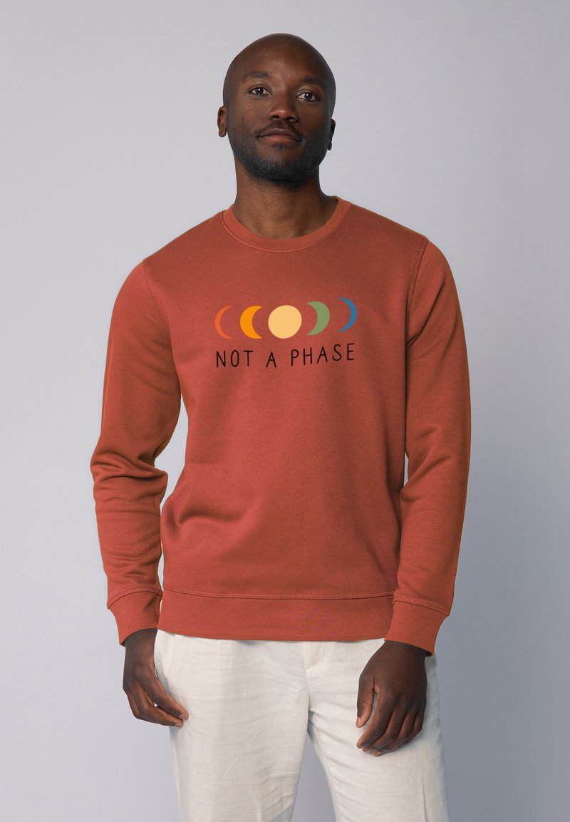 Roestkleurige sweatshirt van een gestructureerde stof, met een grafische print van cirkelvormige vormen in verschillende kleuren en de tekst "NIET EEN FASE."