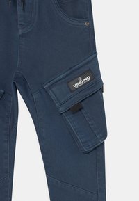 Granatowe dżinsy z kieszenią cargo na udzie, z czarną metką z napisem "Vingino for the love of denim."
