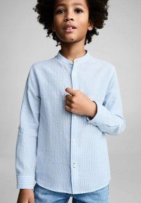 Camicia a righe azzurro chiaro con colletto a banda, davanti con bottoni e maniche lunghe, realizzata in un morbido tessuto testurizzato. Indossata con jeans.