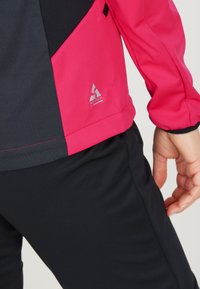Tæt siddende jakke med et farveblokdesign i pink, sort og grå, der har en glat tekstur og WX-TECH-logo nær nederkanten.