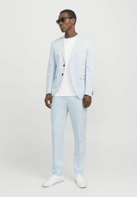 Chaqueta y pantalones de traje azul claro de tejido suave, combinados con una camiseta blanca y zapatillas blancas. Se llevan gafas de sol negras.