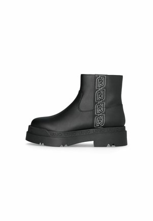 Bottine en cuir noir avec semelle épaisse, logos décoratifs cousus sur le panneau latéral et semelle extérieure texturée.