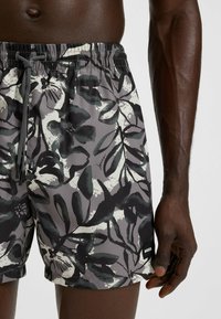 Zwemshorts in een lichtgewicht, rekbare stof met een grijs bloemmotief en groene en zwarte bladeren. Een elastische tailleband met verstelbaar trekkoord.