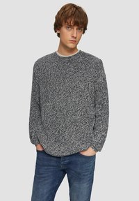 Strickpullover in Schwarz-Weiß-Mix, Rundhalsausschnitt, lockere Passform, strukturierter Muster, langärmlig, kombiniert mit blauen Jeans.