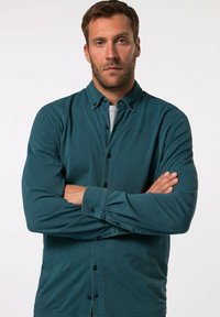 Camicia button-up color verde scuro con maniche lunghe, tessuto texturizzato e colletto classico, con bottoni neri e una vestibilità rilassata.
