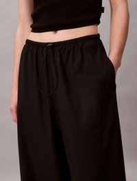 Μαύρο παντελόνι με φαρδιά πόδια και ελαστική μέση, με κορδόνι ρύθμισης και πλαϊνές τσέπες. Λείο ύφασμα με ματ φινίρισμα.