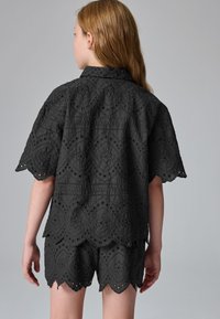Sort broderet bluse med blomsterprints og bølgede kanter, kombineret med matchende shorts i samme materiale og design.