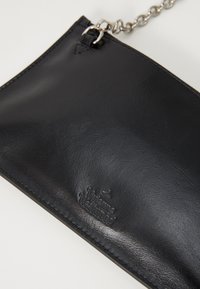 Must mustra nahkainine ümbrik, millel on sile tekstuur, hõbedane kett rind ja reljeefne brändi logo. Ristkülikuline kuju minimalistliku disainiga.