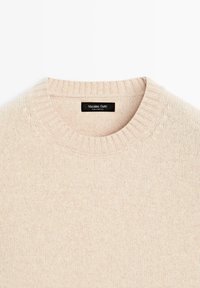 Beżowy sweter dzianinowy z prążkowanym okrągłym dekoltem. Posiada gładką fakturę oraz naszywkę wszytą przy kołnierzu, oznaczoną "Massimo Dutti."