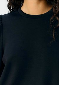 Mustapaita, jossa on pyöreä kaula-aukko, tekstuuriset puffihihat ja sileä kangas. Ei näkyviä kuvioita tai erottuvaa varusteita.