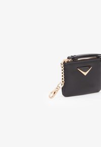 Piccola borsa in pelle nera con zip dorata, logo triangolare dorato e catena decorativa dorata, su sfondo bianco.