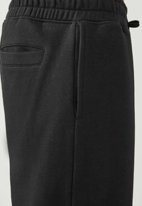 Pantalones jogger negros fabricados en una suave mezcla de algodón, con una cinturilla elástica, bolsillos laterales y una superficie suave y texturizada.
