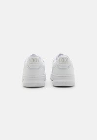 Valged nahast spordijalatsid sileda pinnaga, millega kaasneb kummist talla, ja "L001 LACOSTE" bränding, mis on sisse pressitud kanna külge.