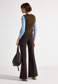 Maglione senza maniche marrone a maglia sopra una maglietta a maniche lunghe azzurro chiaro, abbinato a pantaloni svasati marrone scuro e scarpe con tacco verdi. Borsa nera con texture.