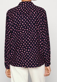 Camicia navy con maniche lunghe caratterizzata da un motivo a cuori rosa, colletto a punta e orlo dritto. Tessuto morbido.