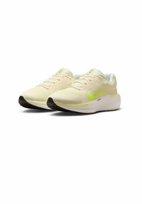 Un paio di scarpe da corsa Nike giallo chiaro con swoosh verde neon e suole nere su uno sfondo bianco.