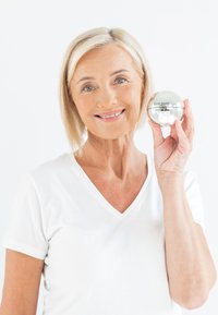 Round silver skincare jar with embossed logo, held by a person. Smooth, reflective surface, minimal design on a white background.