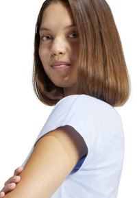 Maglietta azzurra chiara a maniche corte con scollatura rotonda. Il tessuto morbido cade delicatamente sulle spalle. Capelli castani naturali acconciati a caschetto.