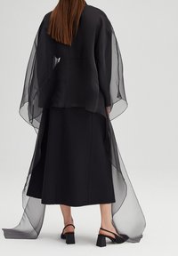 Sort lagdelt outfit med en gennemsigtig, flydende kappe over en struktureret kjole. Skørtet er ankel-langt og har et rent, minimalistisk design.
